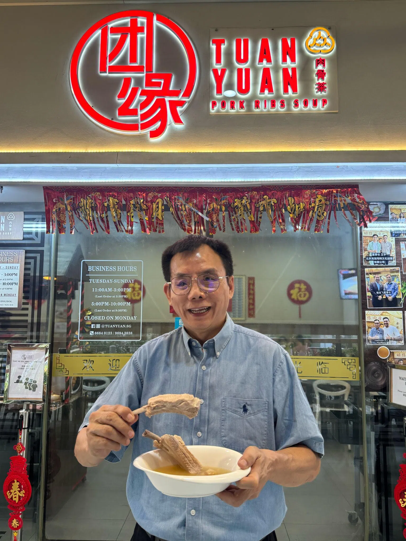 亚华肉骨茶创办人魏松濠在其子女所经营的团缘肉骨茶门市前。 （受访者提供）