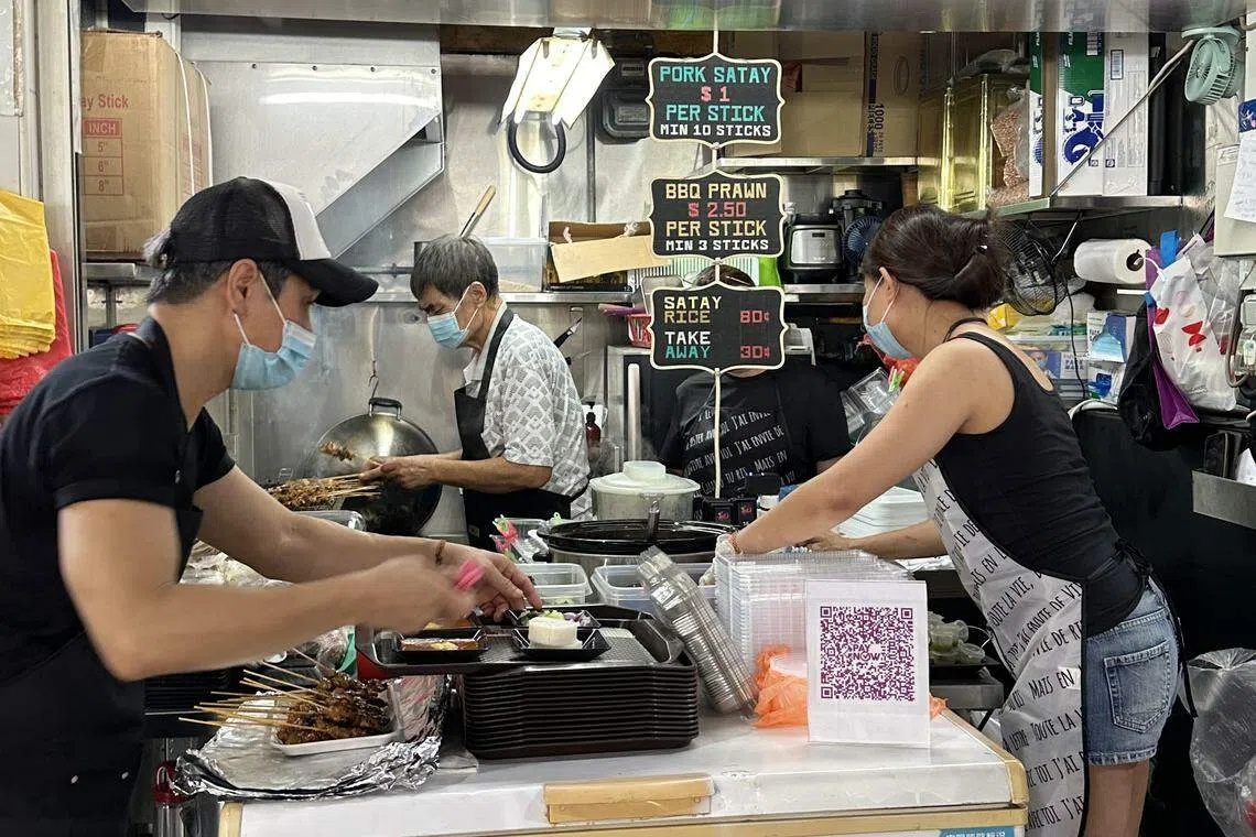 翁文益在档口内烤沙爹，洪添成在外处理订单，另有两人在档口帮忙。（齐鲁摄）