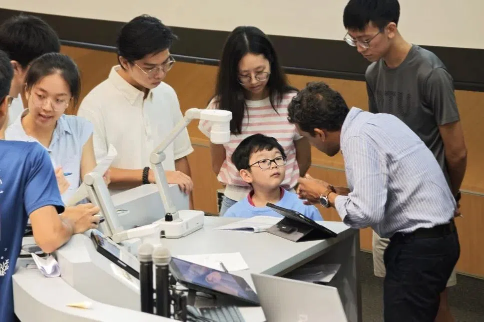 几乎每一节课结束后，关颖恩都会排队向讲师苏莫德博士请教自己听不明白的概念。小小的身影，凑在同学们之间，积极又好学的态度让人印象深刻。（南洋理工大学提供）