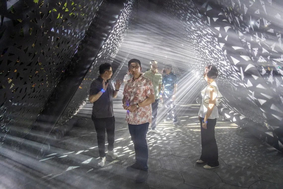国家发展部长徐芳达（中）出席“照亮新加坡”开幕夜，穿行在瑞士艺术团队Encor Studio创作的灯光艺术装置“切片”中。这个装置是灯光照在厚重的织物上，穿过无数三角形的孔洞，照进黑暗的长廊，让公众漫步于长廊内，感受光影变幻。（吴先邦摄）