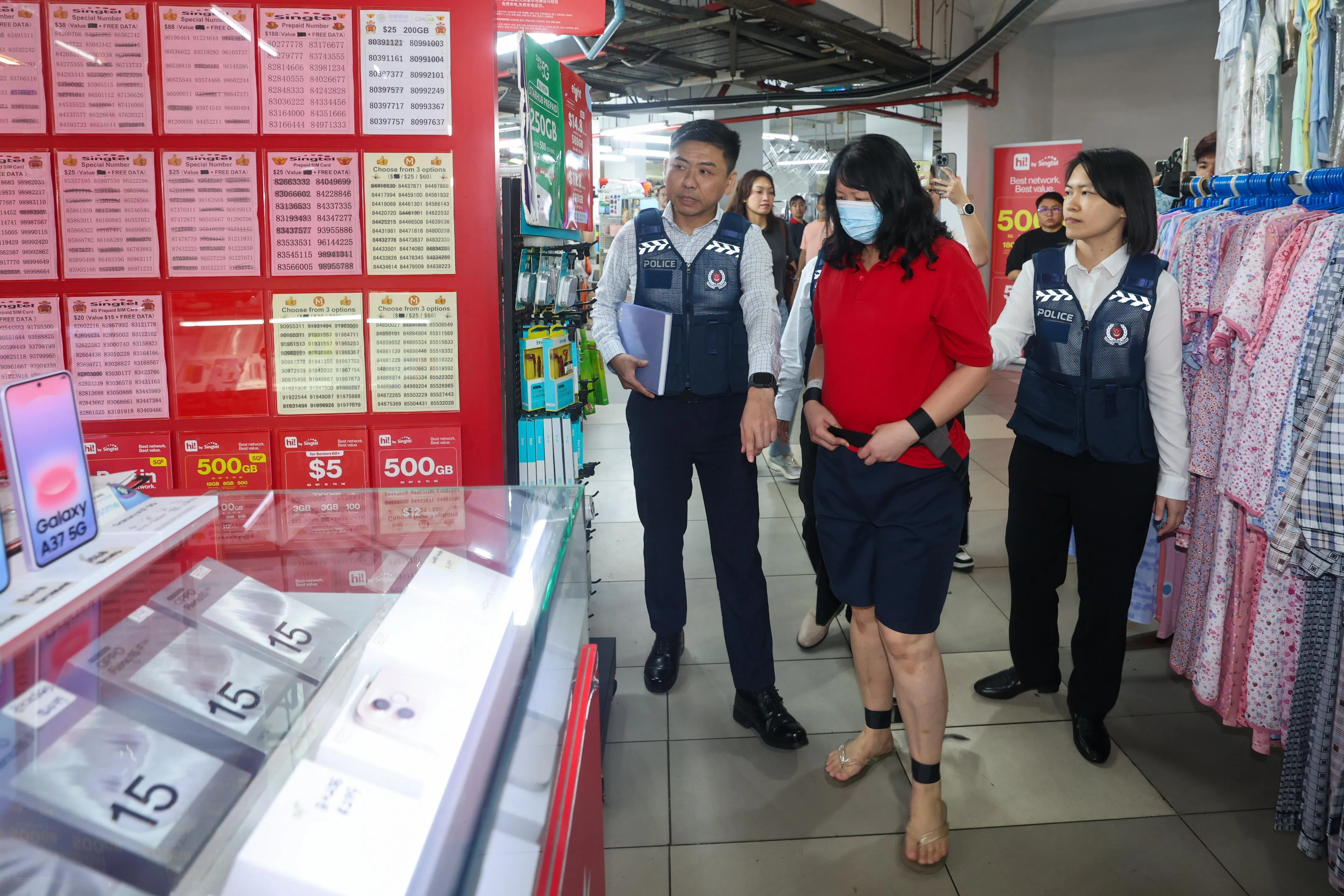 陈珠琴（红衣者）被押到文礼购物中心的一家手机店，在现场逗留约三分钟后，便被押上警车离开。（陈渊庄摄）