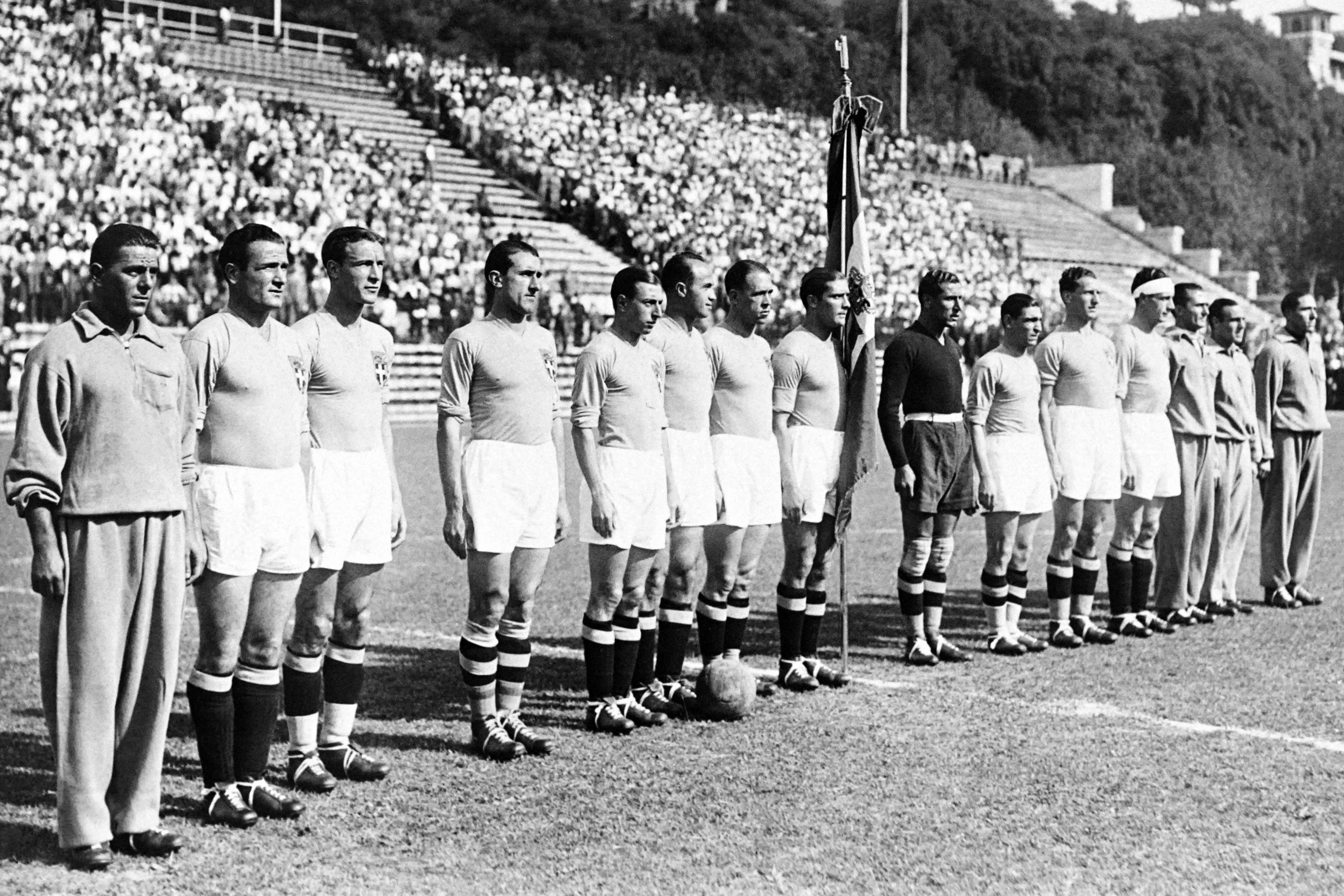 1934年世界杯是历史上第二届世界杯，也是欧洲首次举办世界杯。东道主意大利最终夺得冠军，并在1938年的法国世界杯成功卫冕，成为首支蝉联世界杯冠军的球队。图为意大利传奇前锋、队长梅亚扎（中，持队旗者）与意大利队在1934年世界杯比赛开始前聆听国歌。（法新社）