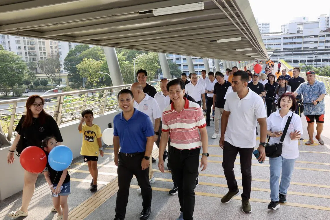 国家发展部长李智陞（中左，蓝衣）和负责南洋区事务的西海岸集选区议员洪维能（中右，红白衣）以及大约1000个居民，星期六一早率先从裕廊西组屋区踏上跨越泛岛快速公路新的行人天桥，走到裕廊创新区。（邝启聪摄）