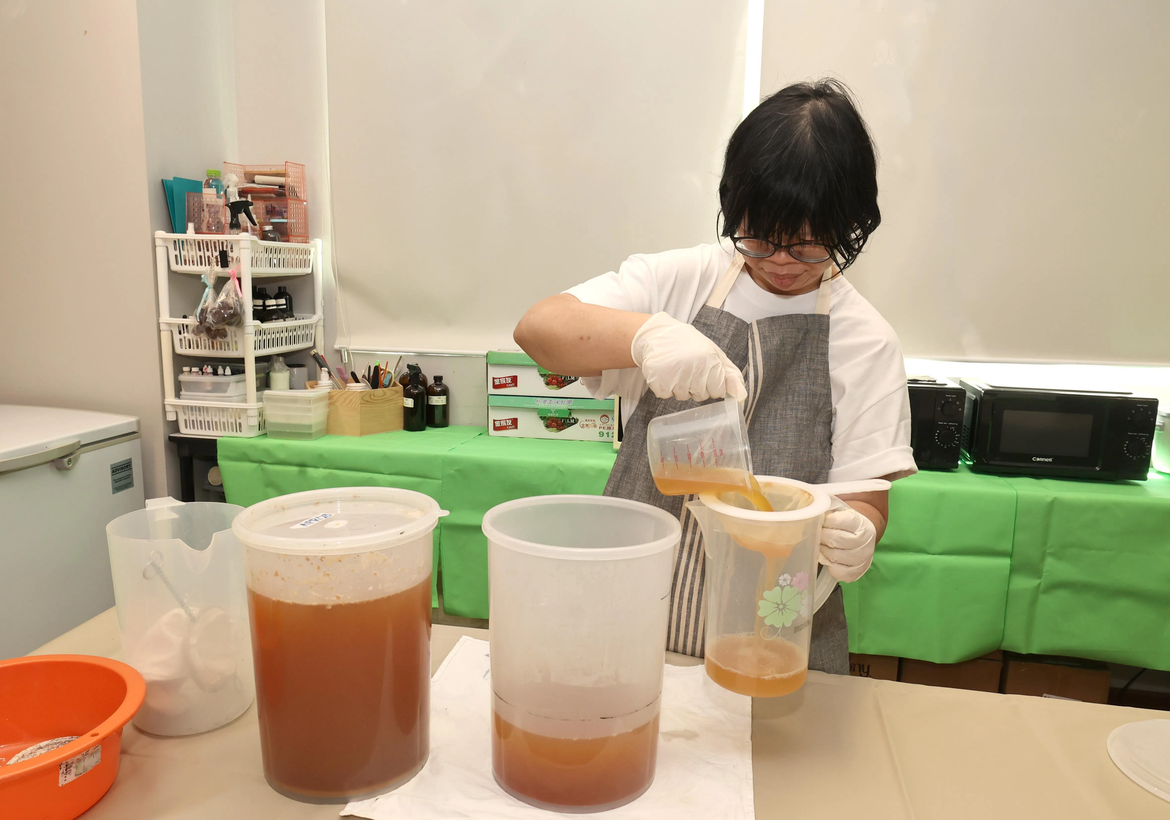 第二步骤是将橙皮、黑糖和水混合，等待发酵。罗梓菱负责第三步骤，使用金属滤网将发酵容器中的霉菌和杂质过滤出来，再使用网状滤网和咖啡滤纸各别过滤一次。（周国威摄）