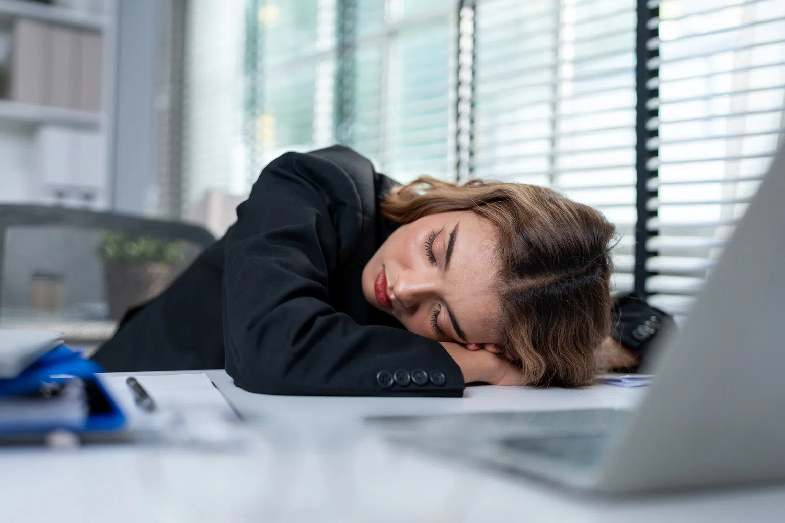 Office worker resting her head on a desk due to fatigue and migraine symptoms.