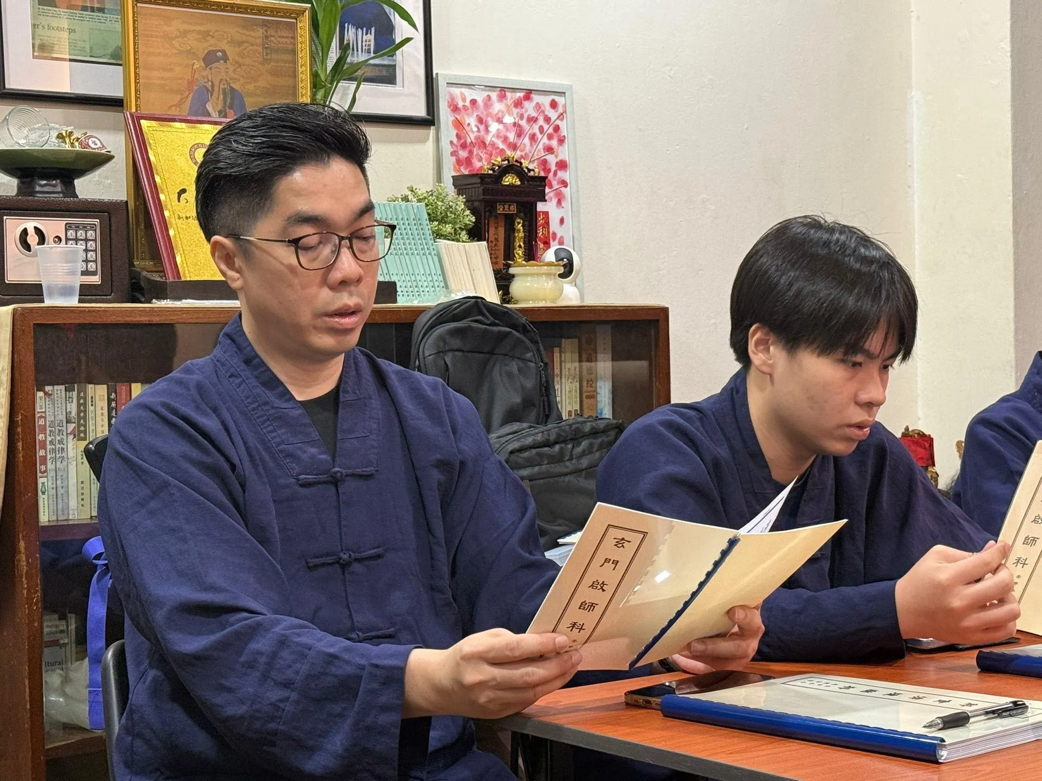 王锦汶（左）与儿子王鼎翔并肩学习粤语诵经；王鼎翔会在科仪本上做笔记，帮助掌握发音和节奏。（杨慧莉摄）