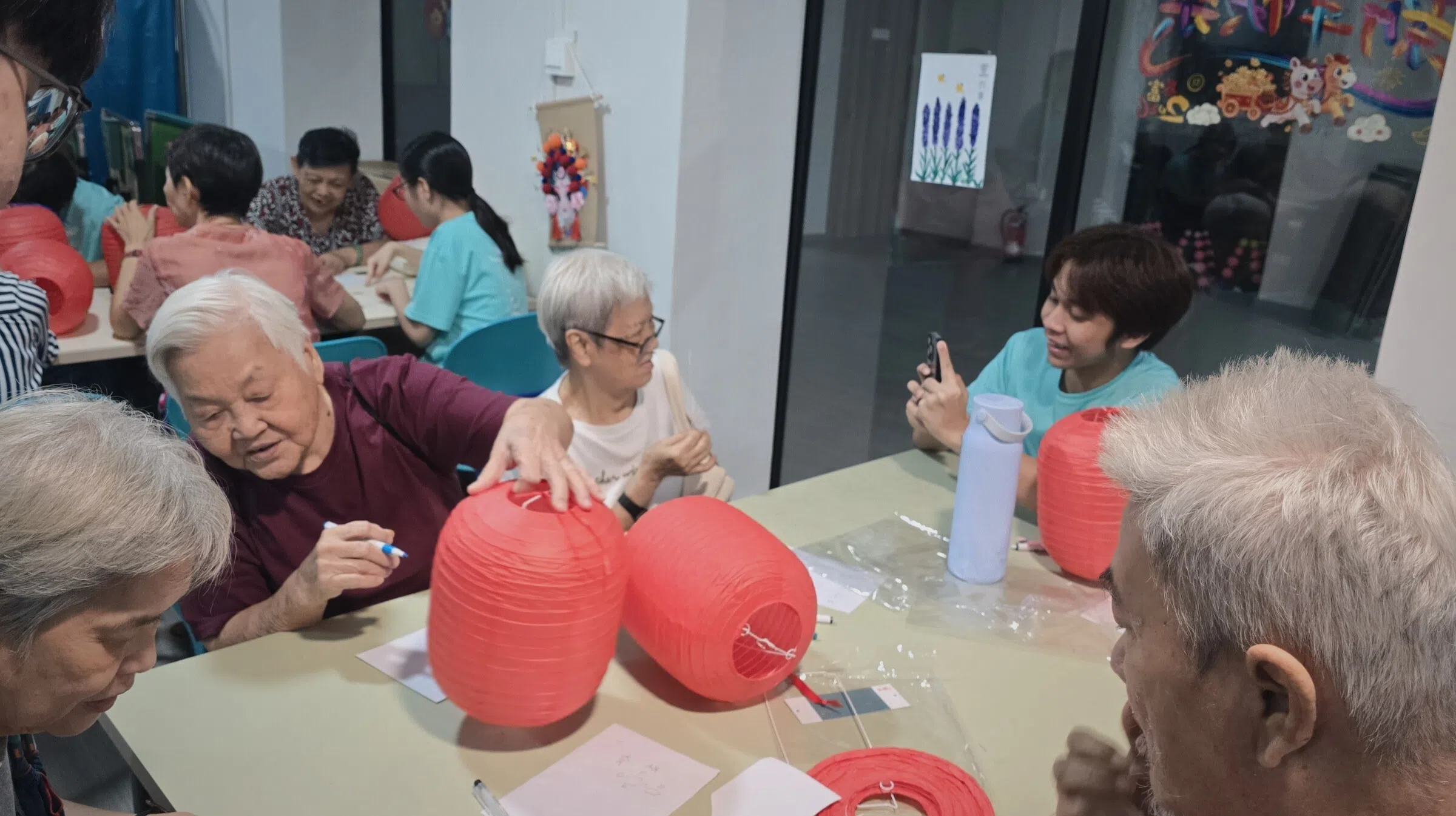 “灯谜大作战”环节中，长者用马克笔、心愿卡和贴纸装饰灯笼，学生在一旁为其拍照。（义安理工学院黄佳宇摄）