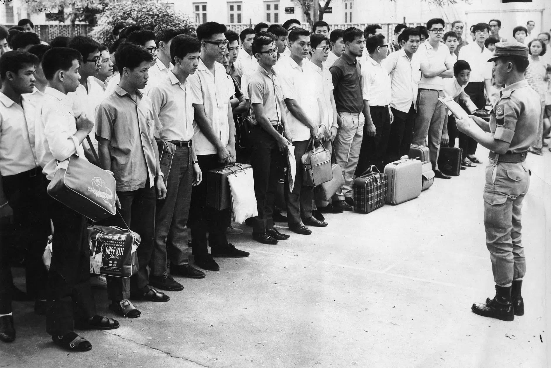 国会于1967年3月通过国民服役法令，年满18岁的男性新加坡公民或第二代永久居民都必须到军队服役22到24个月。服完兵役后，成为战备军人，每年回营受训几个星期。1967年3月，国防部中央人力局开始为适龄青年国民进行登记。7月，第一批9000人的国民服役新兵入伍。图为1968年5月在芳林联络所报到的国民服役青年列队准备出发到兵营。（南洋商报）