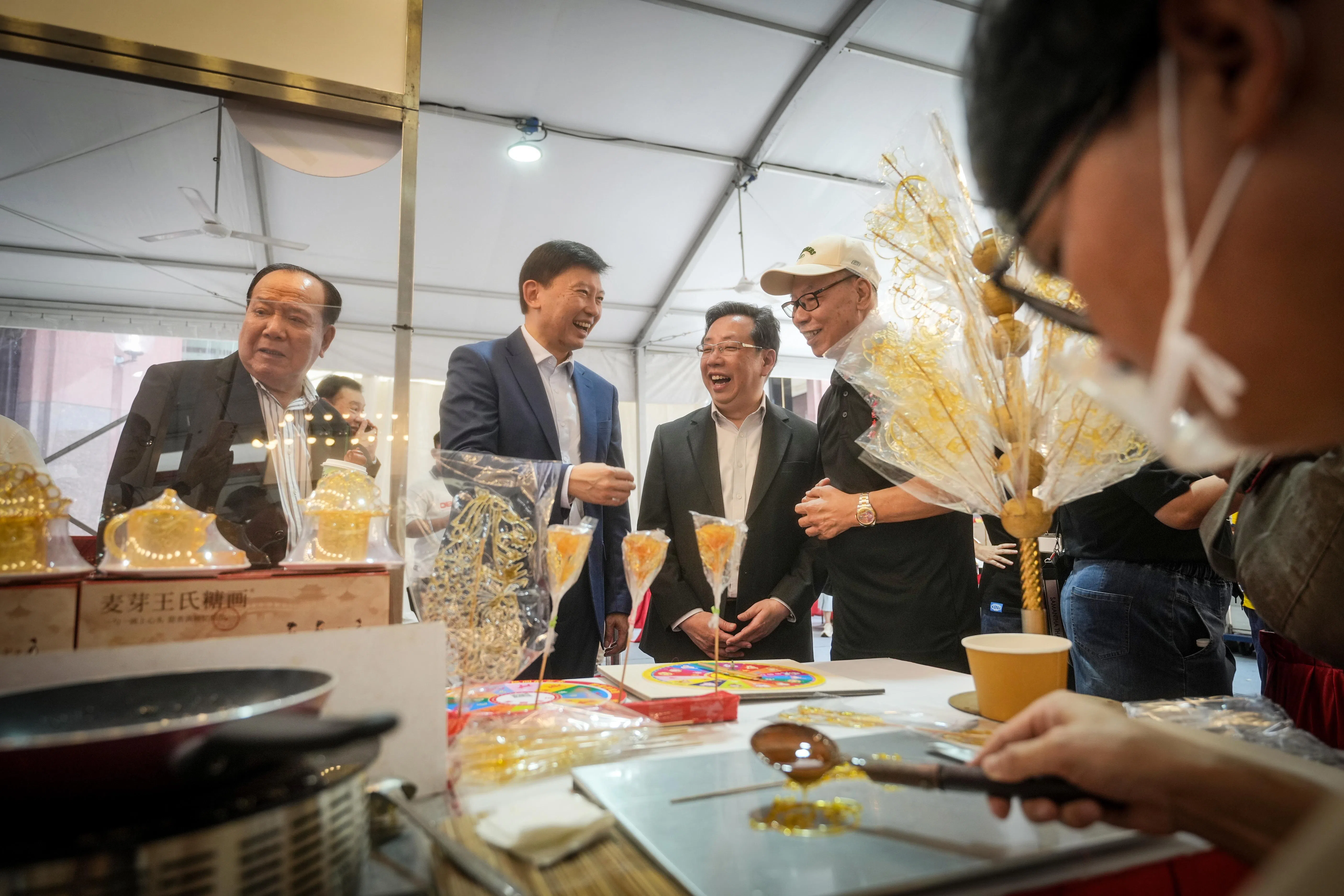 国家发展部长徐芳达（左二）为义安潮州文化美食节主持开幕，走访摊位时，欣赏传统手艺人制作糖画。（谢智扬摄）