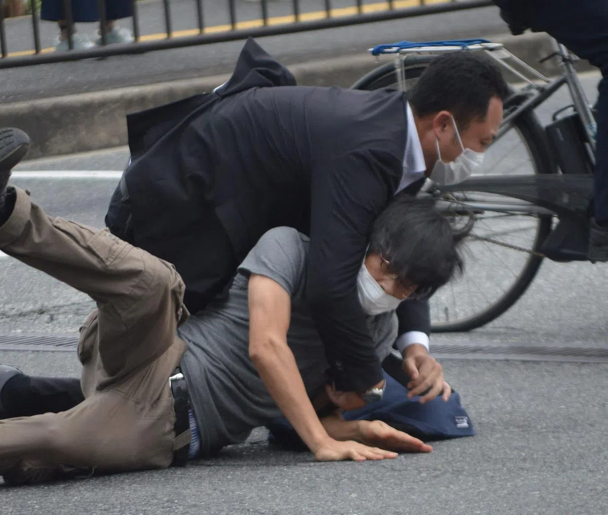 穿黑色大衣的男子制伏涉嫌向安倍晋三开枪的灰衣男子。（法新社/读卖新闻）