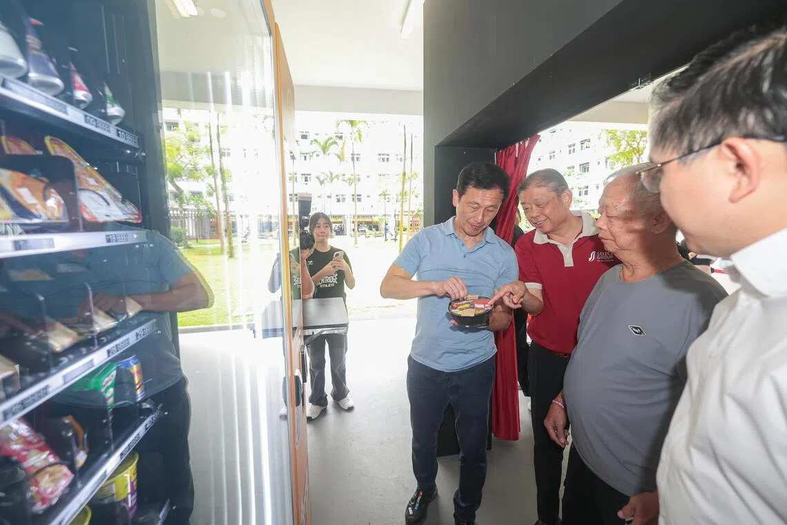 社会政策统筹部长兼保健卫生部长王乙康（左一）说，暖心便当贩卖机是区内援助计划的一部分，协助居民应付生活开销。胜乐集团创办人陈祖坤（左二）向王乙康介绍贩卖机售卖的食品。（李冠卫摄）