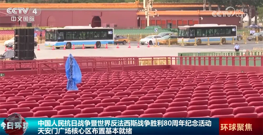 观礼台上的座椅布置选择红色，不仅是和路对面天安门城墙呼应，也与广场周围围合的80面红旗以及红色的花坛布置相得益彰。（央视视频截图）