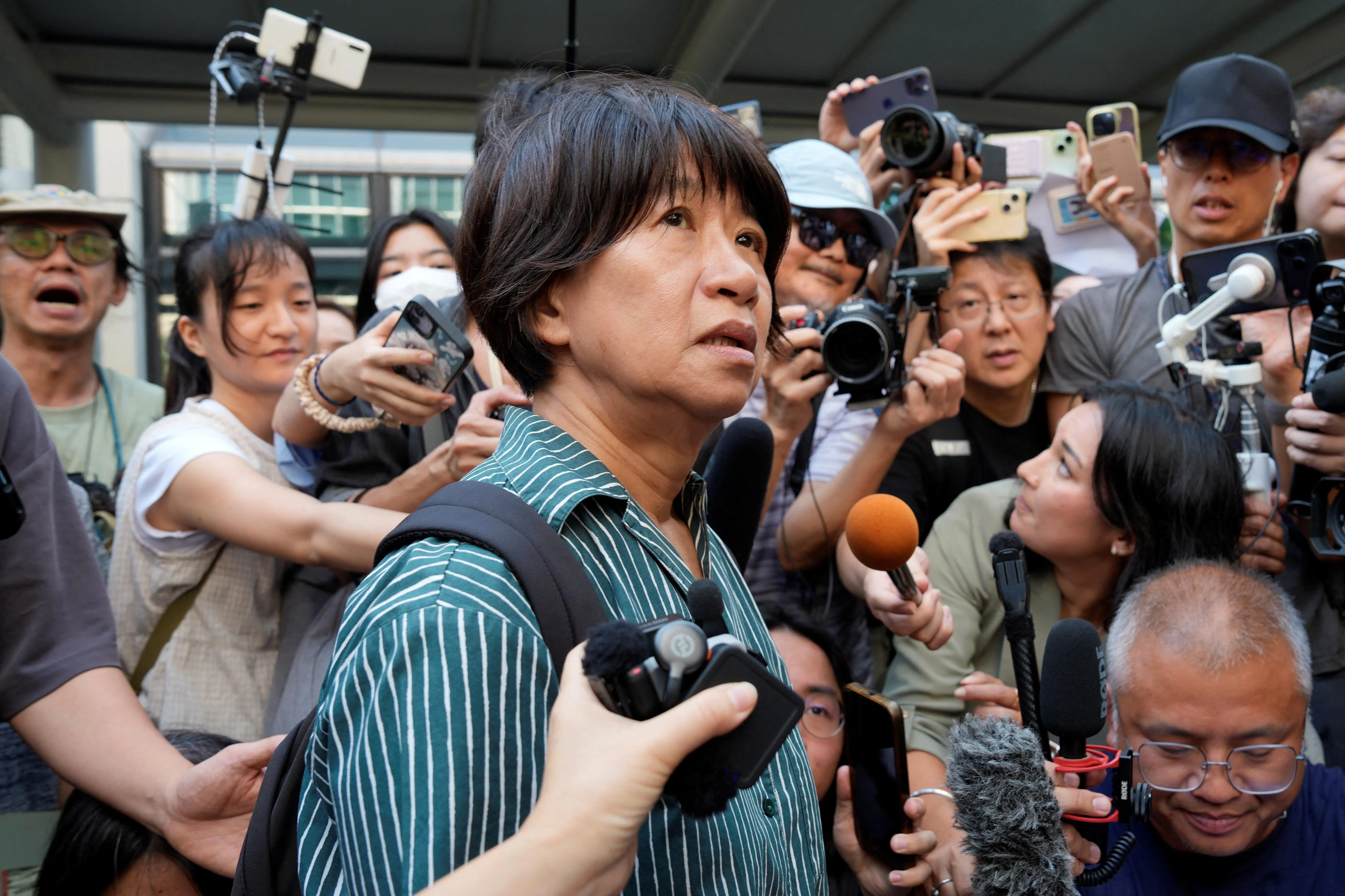 香港支联会煽动颠覆政权案星期五（9月11日）判刑后，记者在西九龙法院外围着访问支联会前主席李卓人的妻子邓燕娥。（路透社）