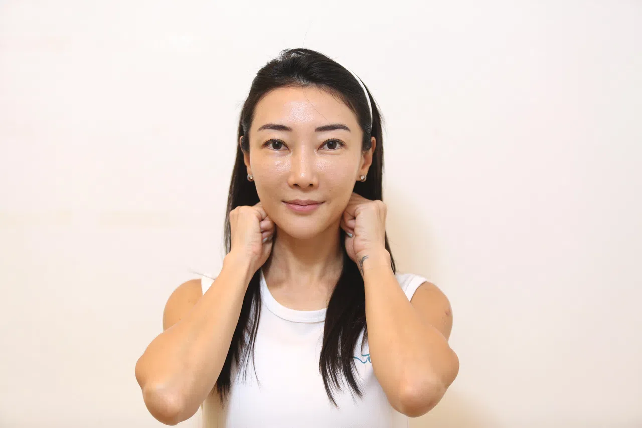 双手握拳放在耳后，由上到下按摩淋巴部位。（李姿仪摄）