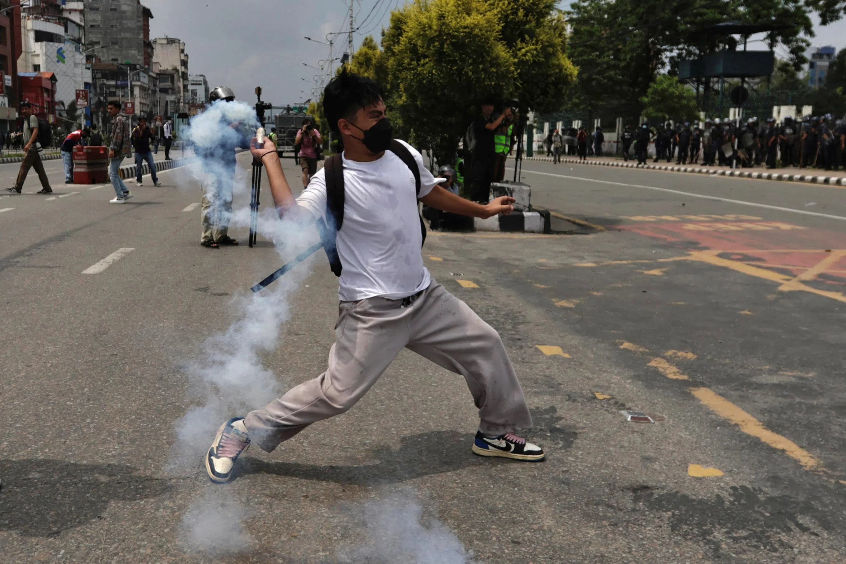加德满都的示威现场，警方与抗议者爆发冲突，一名参与抗议的男子戴着口罩，向防暴警察投掷催泪弹。（路透社）