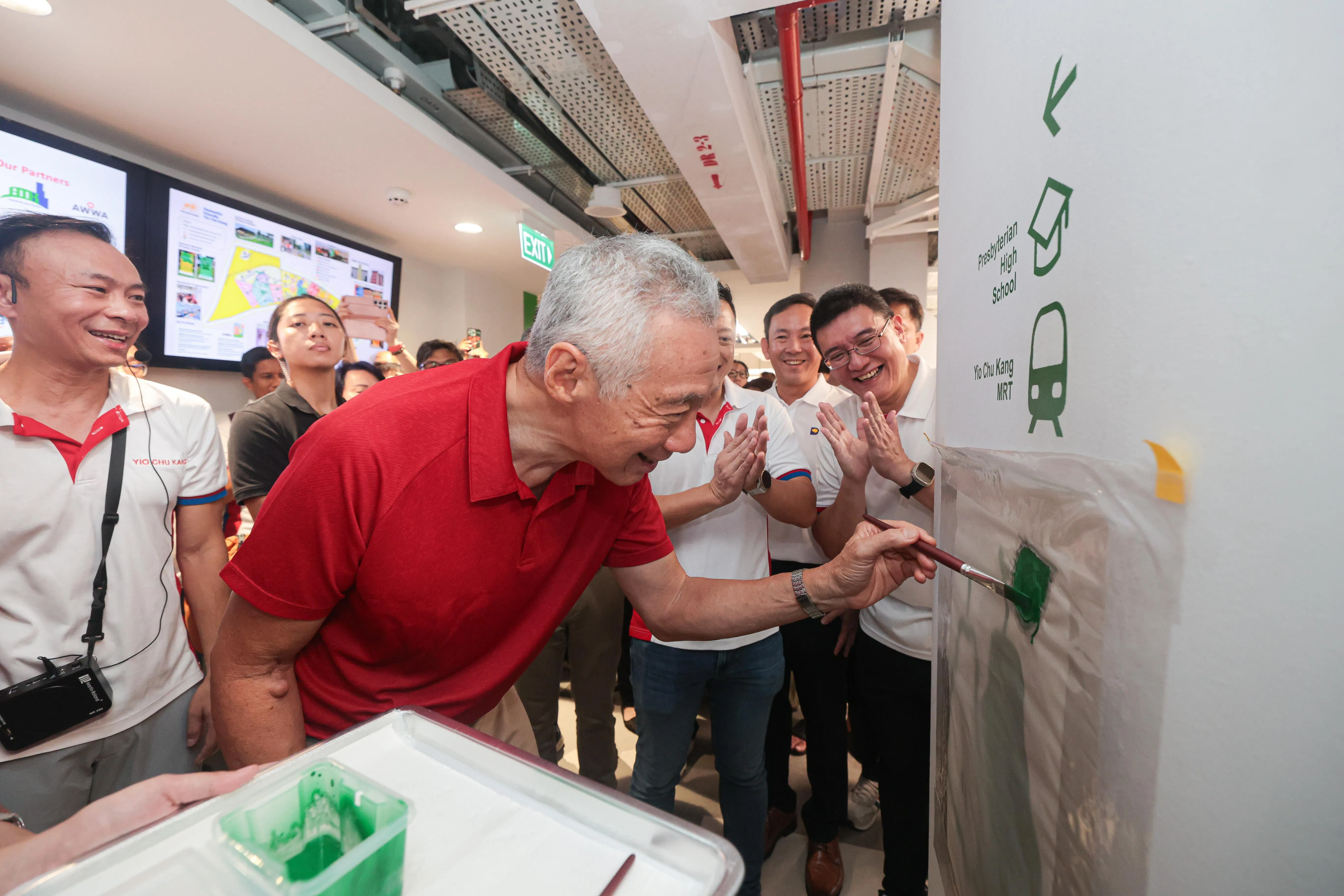 为帮助年长者和失智者更好地认路和寻找设施，俱乐部的路标都更大、更醒目，每一层楼也都以不同鲜艳颜色标识。出席俱乐部开幕仪式的李资政（红衣者）为一楼的梨子图样添上最后一笔。（李冠卫摄）