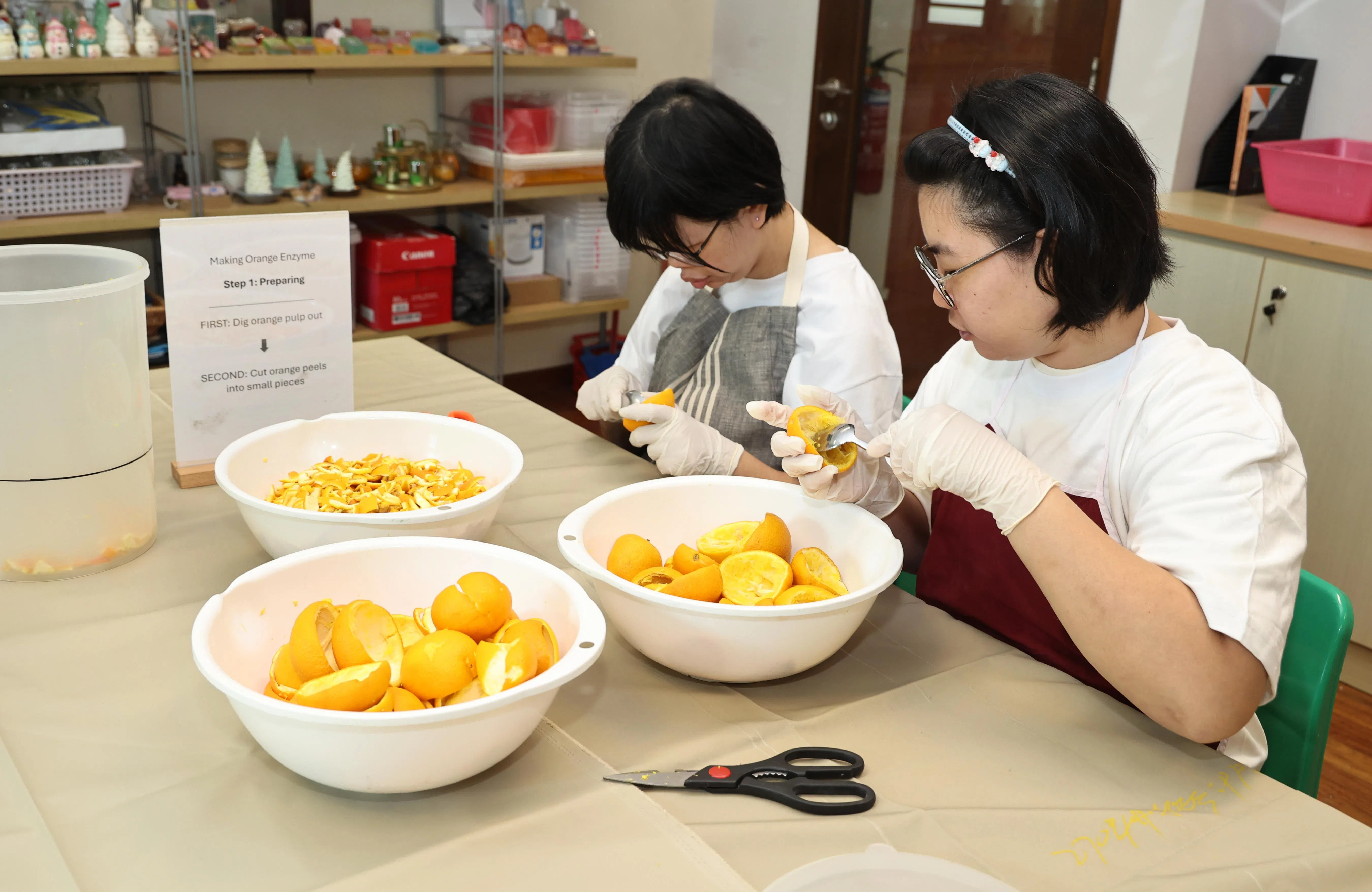 罗梓菱（左） 和翁仪珍（右）在进行制作酵素的第一步骤，挖出果肉和把果皮剪成小片。（周国威摄）