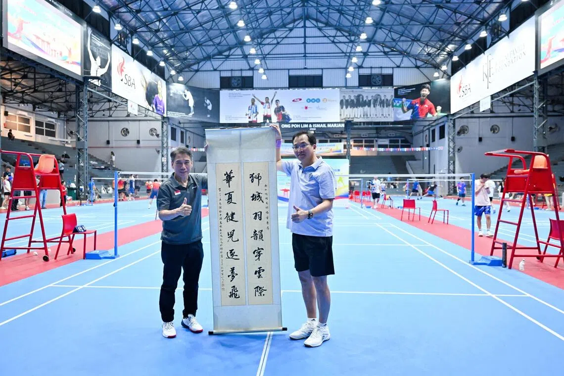 组委会代表戴宏宇（右）为感谢新加坡羽毛球总会对“友谊杯”赛事的大力支持，向羽总会长廖振兴赠送“狮城羽韵穿云际，华夏健儿逐梦飞”卷轴。（主办方提供）