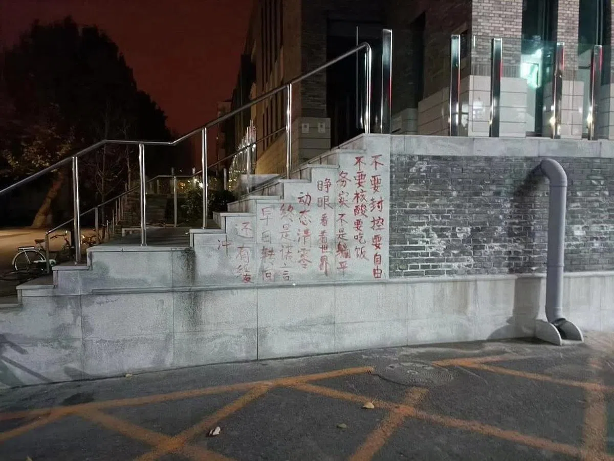 北京大学餐饮综合中心外的楼梯墙上，有红漆书写的“不要封控要自由/不要核酸要吃饭/务实不是躺平/睁眼看世界/动态清零终是谎言/早日转向还有缓冲”抗议口号。（读者提供）