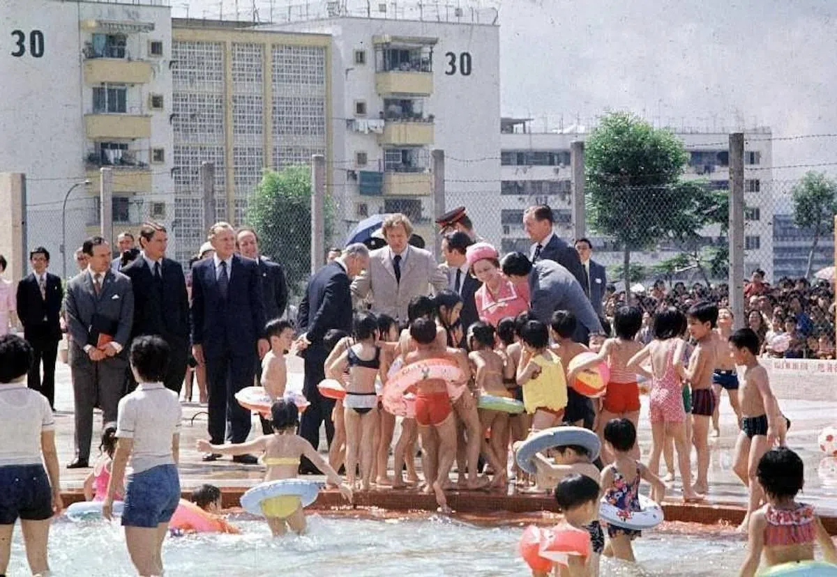 英女王到摩士公园泳池时，一大群小孩好奇地围着她，女王则展露灿烂的笑容与孩子们交谈。 （香港政府新闻处）