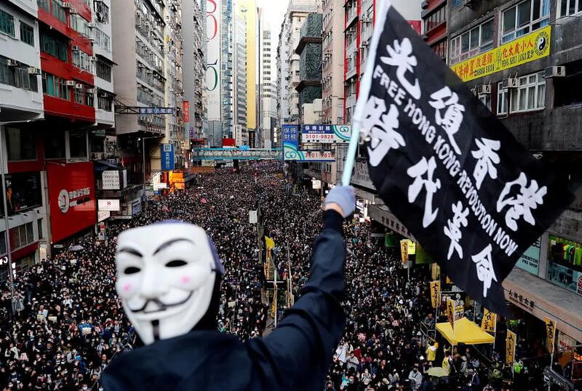 2019年12月8日，一名戴着面具的黑衣男子，在香港一场示威游行中挥舞着印有“光复香港，时代革命”的黑旗。（路透社档案照）