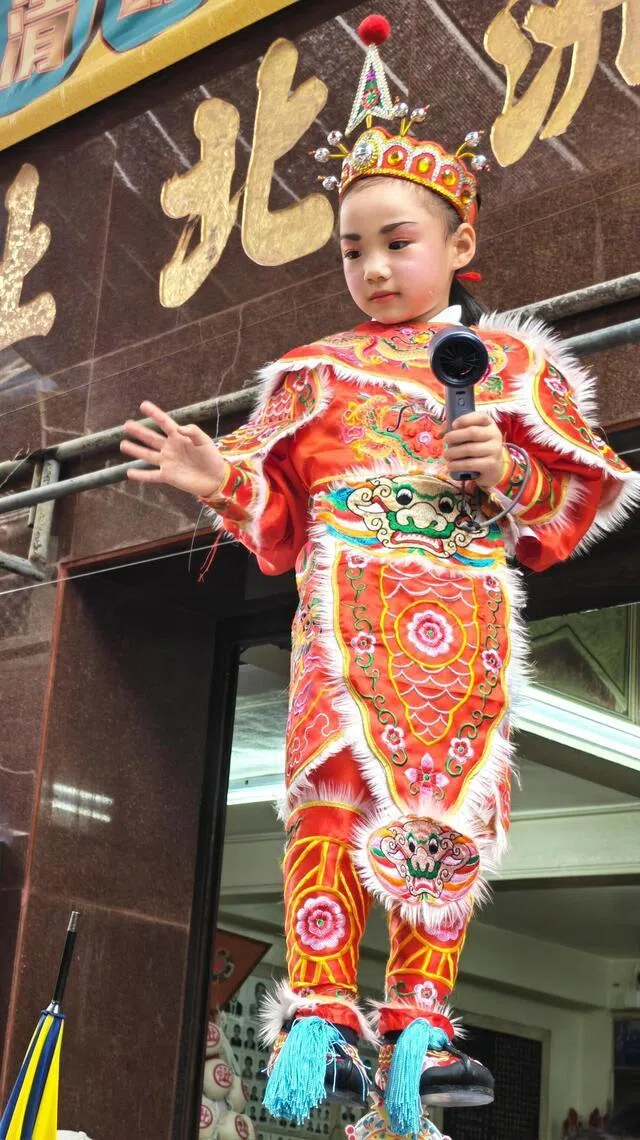 参与飘色巡游的小朋友，很“敬业”地露出可爱笑容和手势。（陈爱薇摄）