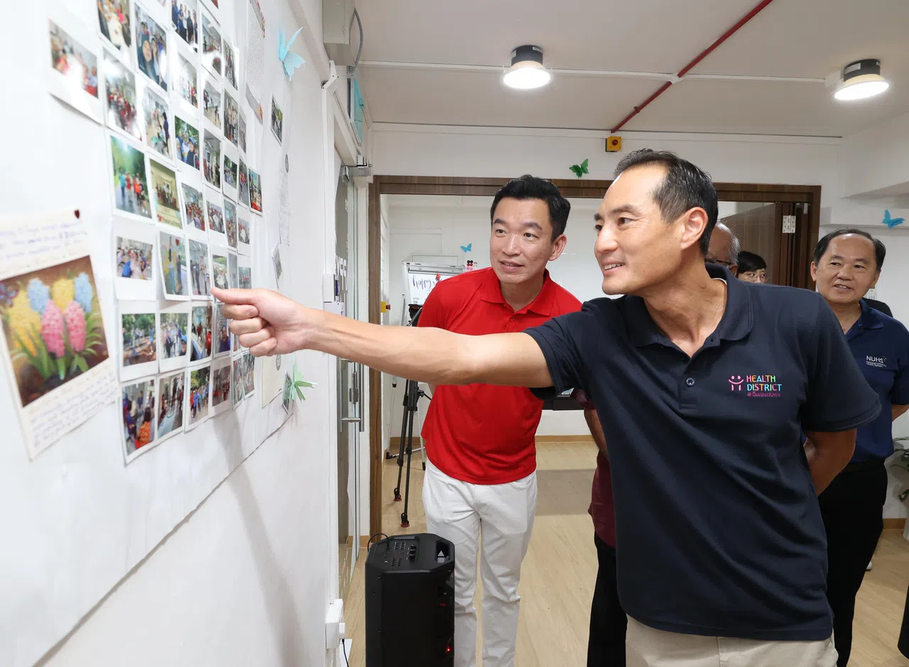 数码发展及新闻部兼国家发展部高级政务部长陈杰豪（前）与女皇镇区基层顾问、文化、社区及青年部兼社会及家庭发展部高级政务次长蔡瑞隆（左）星期六为“美玲好友聚乐部”开幕时，观看中心的活动照片和居民留言。 （唐家鸿摄）