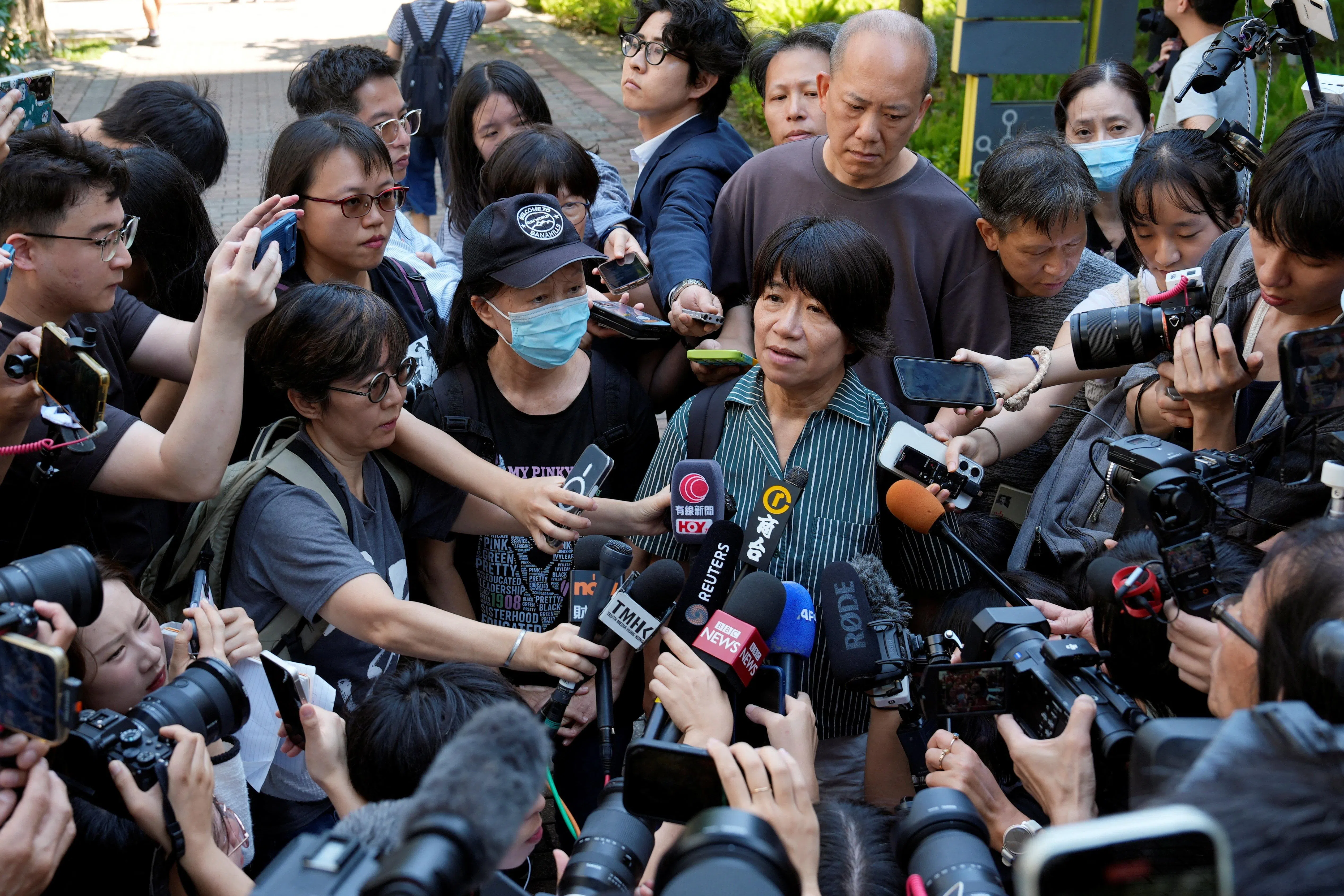 香港支联会前主席李卓人的妻子邓燕娥（中）9月11日在西九龙法院外接受媒体采访，对丈夫的判刑表示感到非常伤心及愤怒。站在她身边、戴着鸭舌帽和口罩的黑衣女子为支联会前副主席邹幸彤的母亲刘华珍。（路透社）