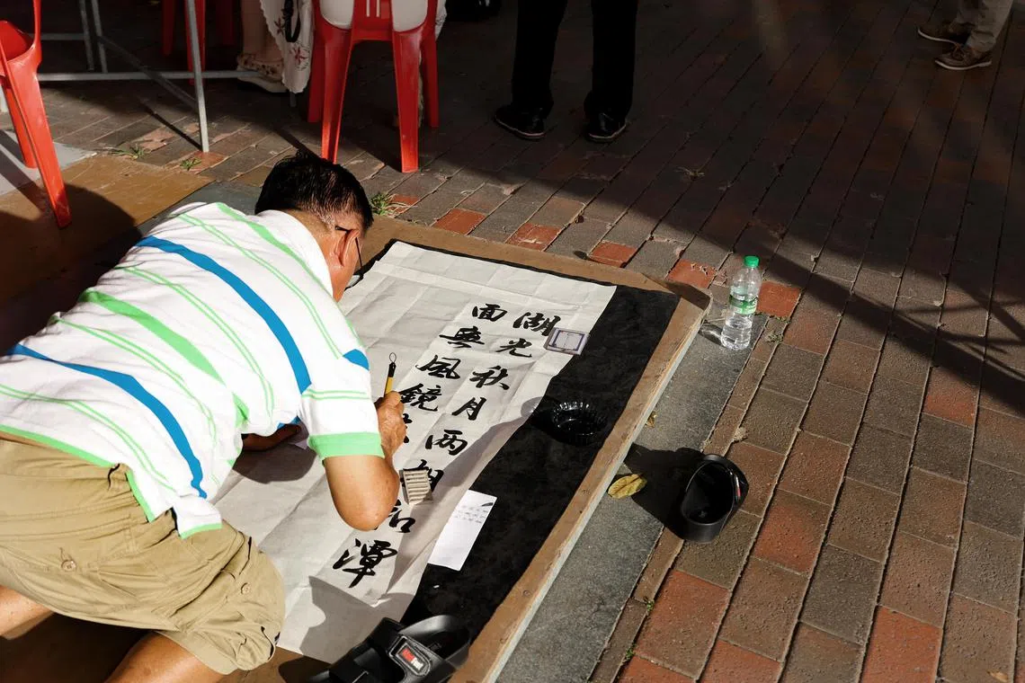 公开组毛笔书法第三名、硬笔书法优秀奖得主陈德利（66岁）现场参赛时，认为桌子限制发挥空间，选择就地挥毫。（陈心媛摄）