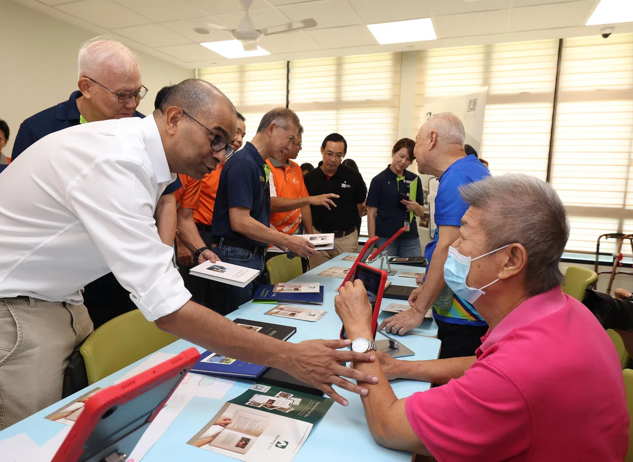 卫生部兼数码发展及新闻部高级政务部长普杰立医生（左一），向参与圣路加乐龄关怀北岸活跃乐龄护理中心黄金岁月回忆录计划的年长者邓水满（右一），了解如何使用人工智能工具，将重要的回忆转化成文字，以有形的方式传承下去。（唐家鸿摄）