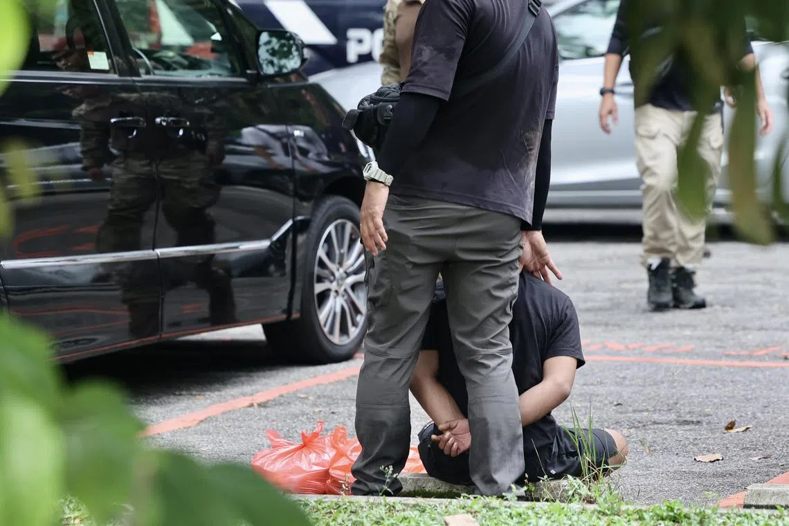 一名嫌犯双手上铐，坐在露天停车场的路缘等待警员进一步指示。（陈斌勤摄）